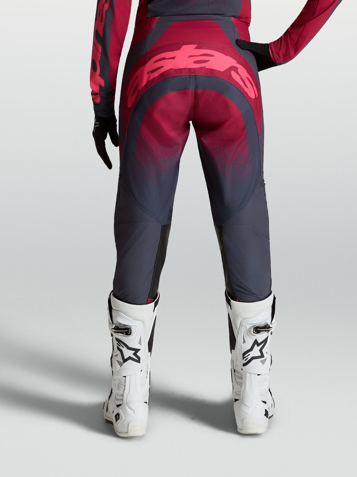 Alpinestars Pantaloni Stella Techstar Swan, pantaloni motocross da donna, grigio e cremisi, vista posteriore su modella con stivali bianchi, abbigliamento off-road ad alte prestazioni.