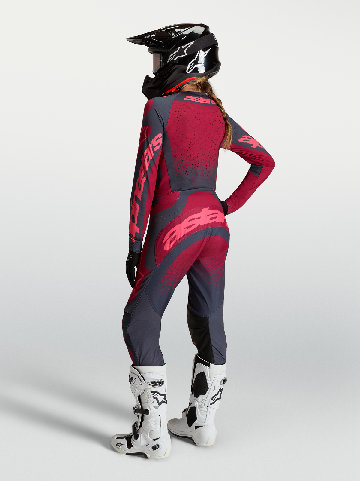 Alpinestars Maglia Stella Techstar Swan e Stella Techstar Swan Gear Set, completo da motocross per donna, rosso e grigio scuro, vista posteriore su modella con casco e stivali bianchi, abbigliamento tecnico off-road