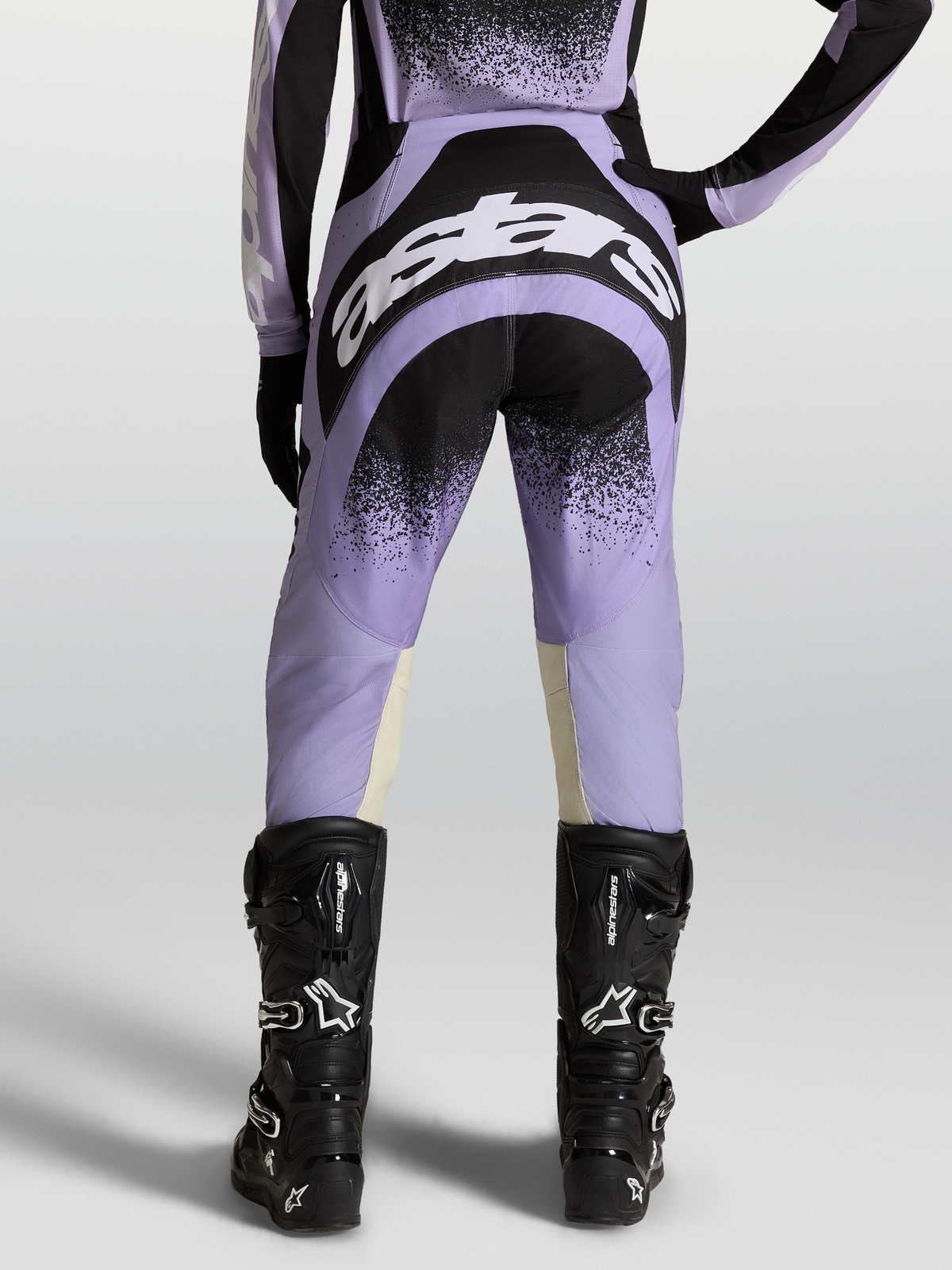 Alpinestars Pantaloni Stella Techstar Swan, pantaloni motocross da donna, viola e neri, indossati con stivali neri.