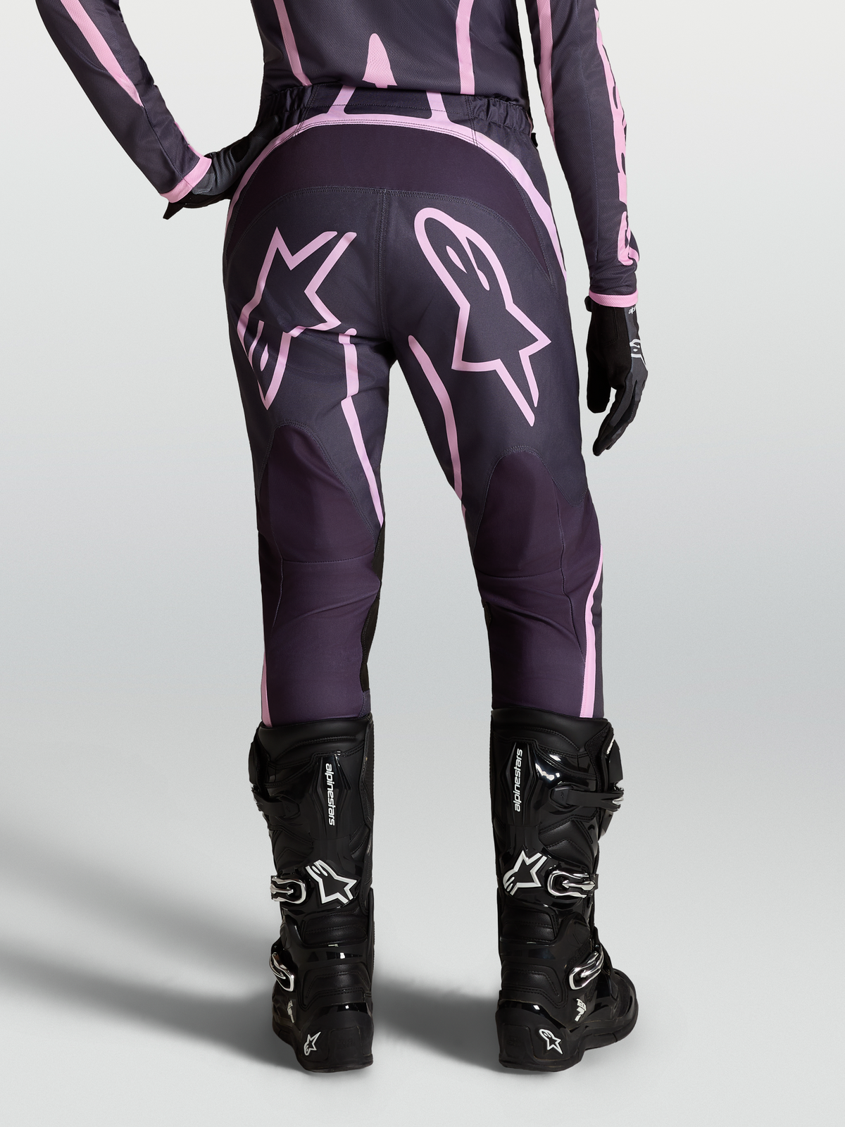 Alpinestars Pantaloni Stella Fluid Apex V2, pantaloni motocross da donna, grigio e rosa, con grafiche a stella e stivali moto neri.
