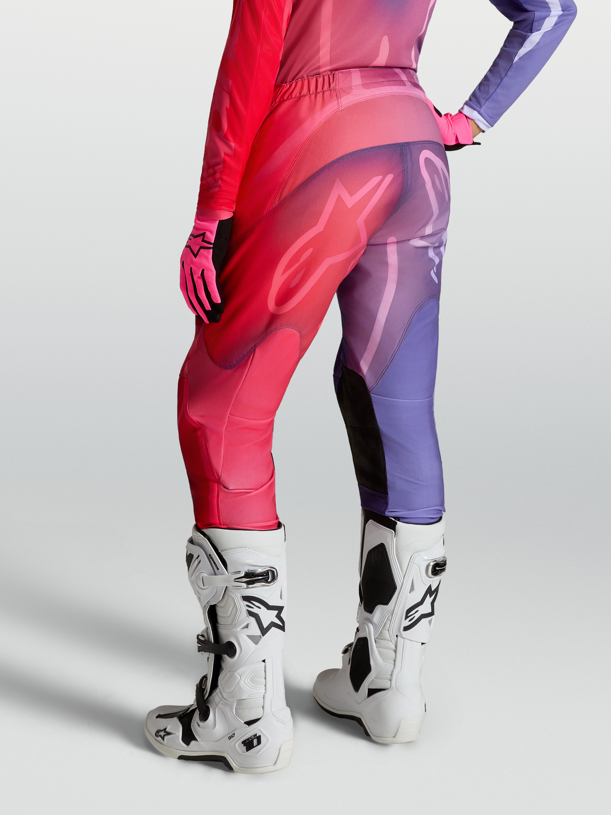 Alpinestars Pantaloni Stella Fluid Kepler, pantaloni motocross da donna, viola e rosso, gambe precurvate, pannelli stretch, indossati con stivali bianchi.
