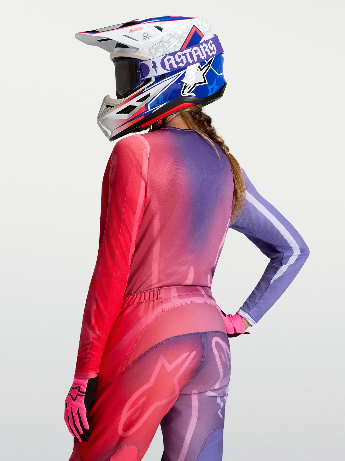 Alpinestars Maglia Stella Fluid Kepler, maglia da motocross da donna, gradiente viola e rosso, indossata su modello con casco e guanti coordinati, abbigliamento fuoristrada tecnico e traspirante