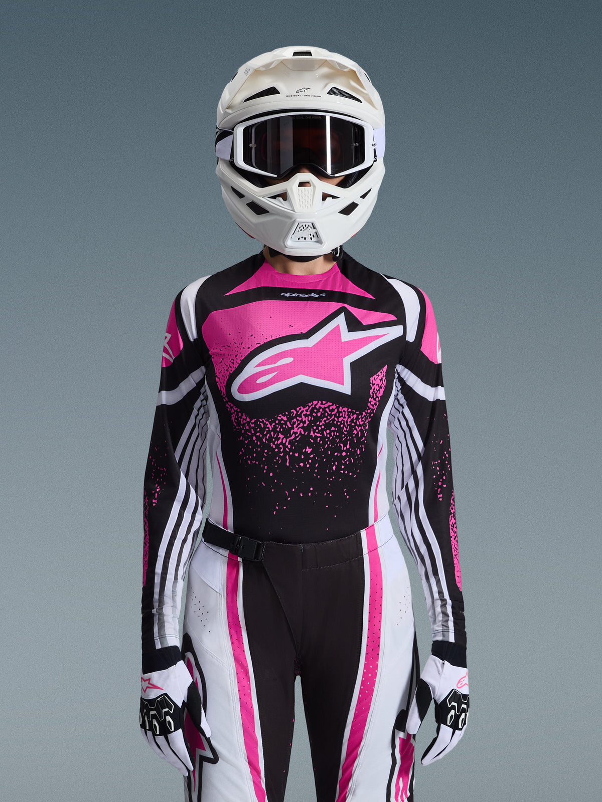 Alpinestars 2026 Stella Techstar Nomur Gear Set, completo da motocross da donna, rosa, nero e bianco con grande logo a stella, con maglia, pantaloni e guanti coordinati e un casco bianco, vista frontale su sfondo grigio