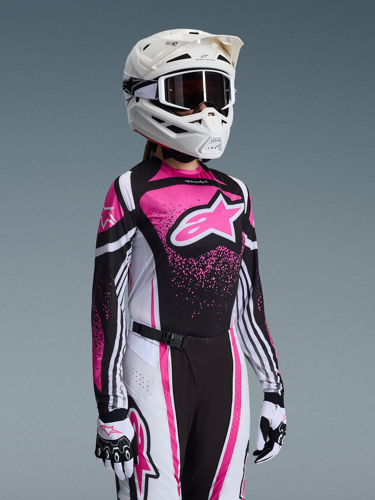 Pilotessa di motocross con il completo Alpinestars 2026 Stella Techstar Nomur in rosa, nero e bianco; maglia con grande logo a stella rosa, pantaloni coordinati con fibbia magnetica, casco bianco con maschera e guanti bianchi e neri.