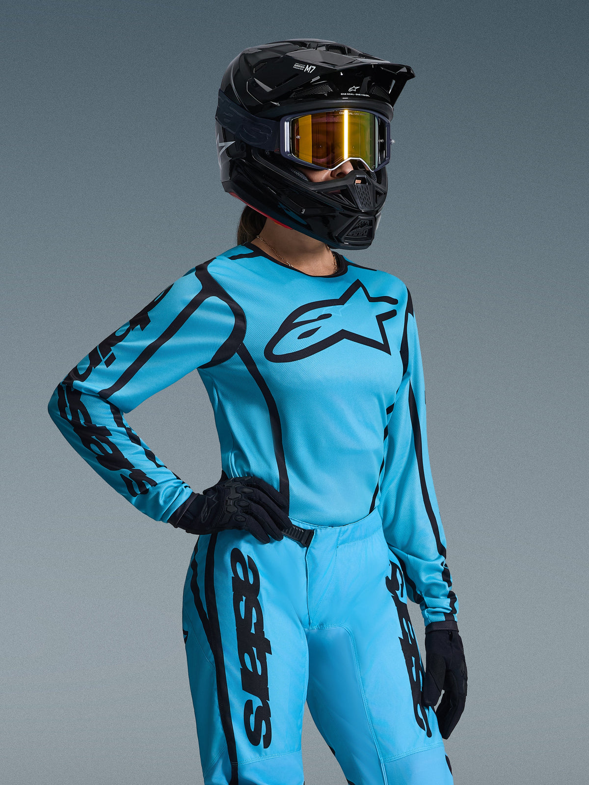 Set Equipaggiamento Alpinestars Stella Fluid Apex Donna 2026, blu brillante e nero, maglia e pantaloni da motocross con branding nero, indossato con casco nero, occhiali a specchio dorati e guanti neri, vestibilità specifica femminile per corse fuoristrada