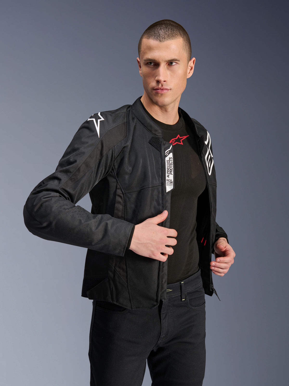 Giacca Alpinestars Viper Air V4, giacca da moto in tessuto nero, indossata da un modello uomo con jeans neri e base layer, zip aperta che mostra le etichette Tech-Air Ready e Alpinestars Protects, loghi bianchi sulle spalle, pannelli in mesh per il flusso d'aria
