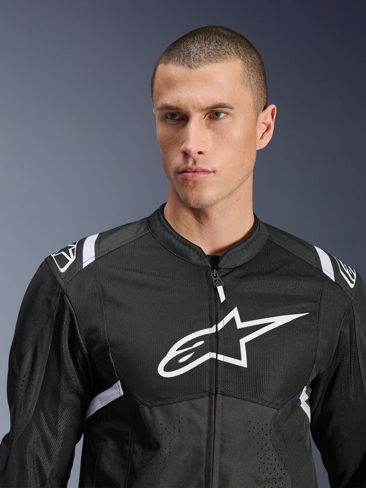 Giacca Alpinestars T-SPS Air V2, giacca da moto in tessuto, nero e bianco, con grande logo bianco sul petto e pannelli in mesh, vestibilità sportiva performante indossata da un modello