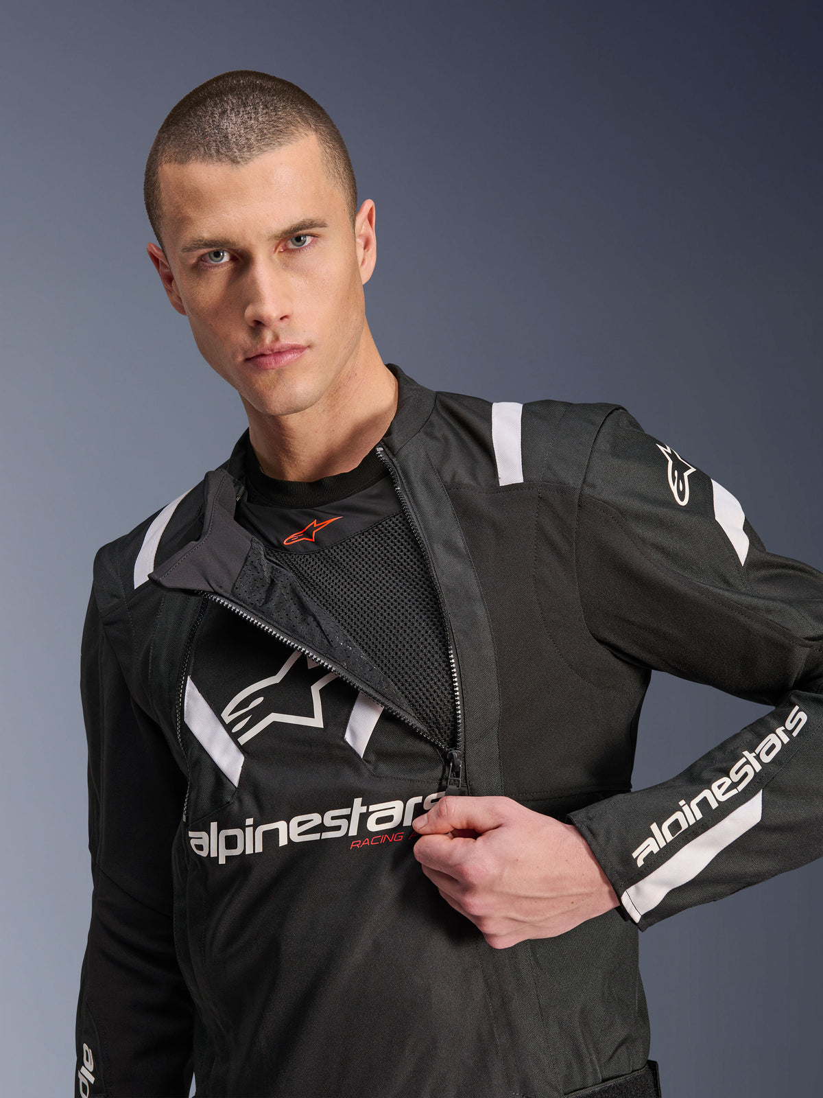 Alpinestars Giacca T-Stunt Air, giacca da moto nera e bianca, modello uomo che mostra il pannello frontale modulare parzialmente aperto rivelando gli strati in rete per il flusso d'aria, loghi Alpinestars bianchi su petto e maniche, design sportivo per la guida su strada