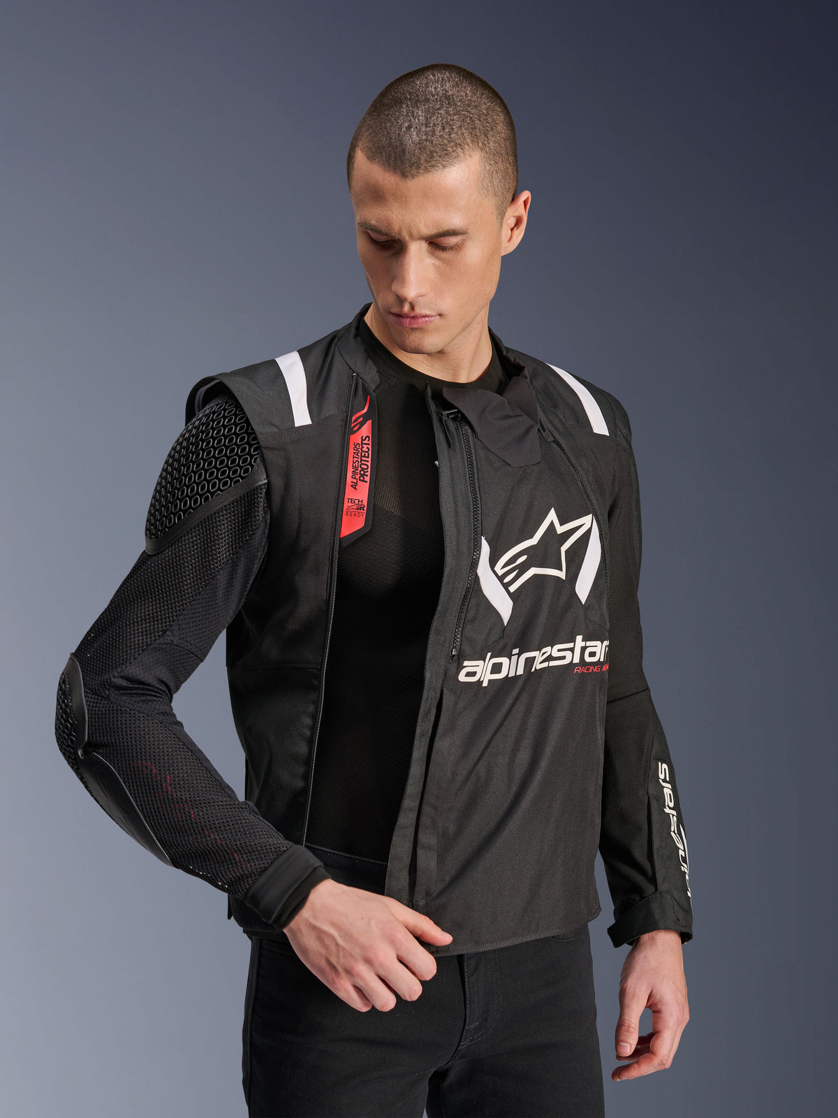 Giacca Alpinestars T-Stunt Air, giacca da moto nera e bianca, indossata da un modello, che mostra la costruzione modulare in mesh e le protezioni interne a vista su spalla e gomito, logo Alpinestars sul petto, predisposizione Tech-Air, taglio sportivo per guida su strada