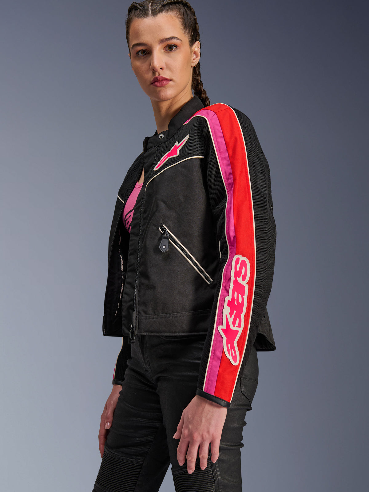Alpinestars Stella T-Dyno Air Jacket, giacca da moto da donna, nero con accenti rosso brillante e fucsia, indossata con pantaloni neri, logo Astars rosa sul petto e sulla manica, vestibilità biker su misura con pannelli in rete per la ventilazione.