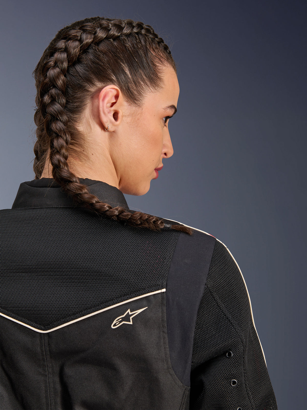 Donna che indossa la giacca Alpinestars Stella T-Dyno Air, vista posteriore ravvicinata focalizzata su spalle e giogo, nera con pannelli in rete 3D traspirante, profili bianchi e piccolo logo Astars, modella con capelli intrecciati, abbigliamento moto urban