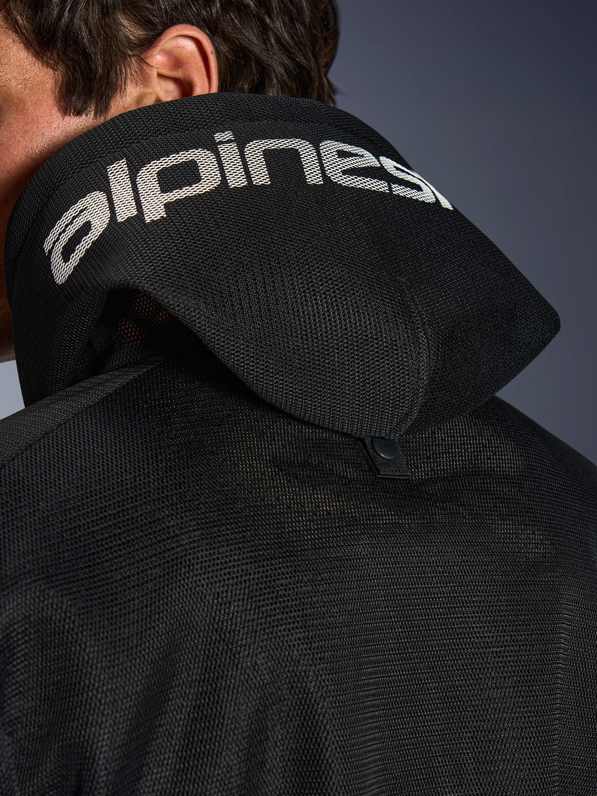 Alpinestars Chrome Superairflow Hoodie, nero, vista dettagliata del cappuccio in mesh 3D con marchio Alpinestars bianco sulla parte superiore, mostra il bottone di stabilizzazione posteriore, abbigliamento da moto in tessuto ventilato per calore estremo