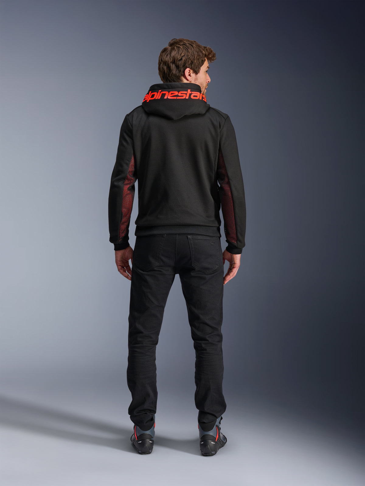 Alpinestars Chrome Air Sport Hoodie, nero e rosso fluo, vista posteriore di un uomo che indossa una giacca da moto casual, con logo Alpinestars rosso sul cappuccio e pannelli in mesh rossi sulle maniche, abbinata a pantaloni neri