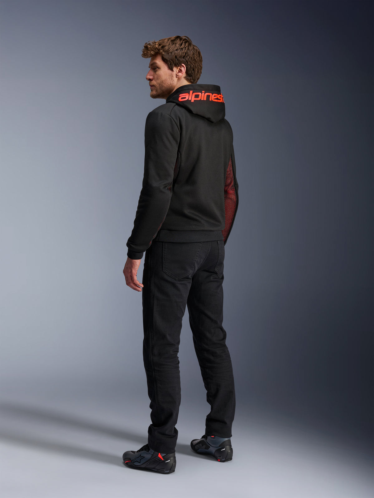 Alpinestars Chrome Air Sport Hoodie, felpa da moto urbana, Nero e Rosso Fluo, vista posteriore con marchio Alpinestars rosso sul cappuccio e pannelli laterali in mesh, indossata con pantaloni da guida neri e calzature tecniche