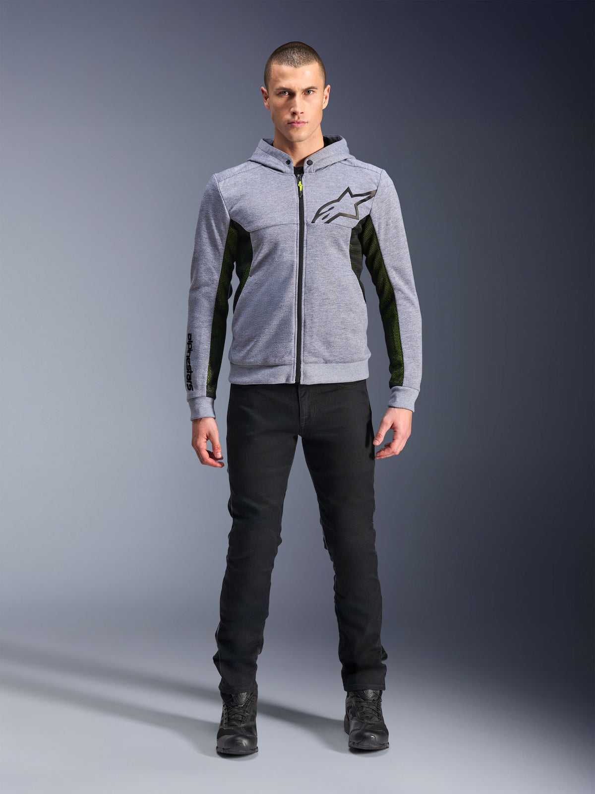 Alpinestars Chrome Air Sport Hoodie, grigio melange e nero, felpa tecnica da moto con pannelli laterali in mesh nero e accenti giallo neon, logo a stella nero sul petto, indossata con pantaloni e stivali neri, stile urban moderno