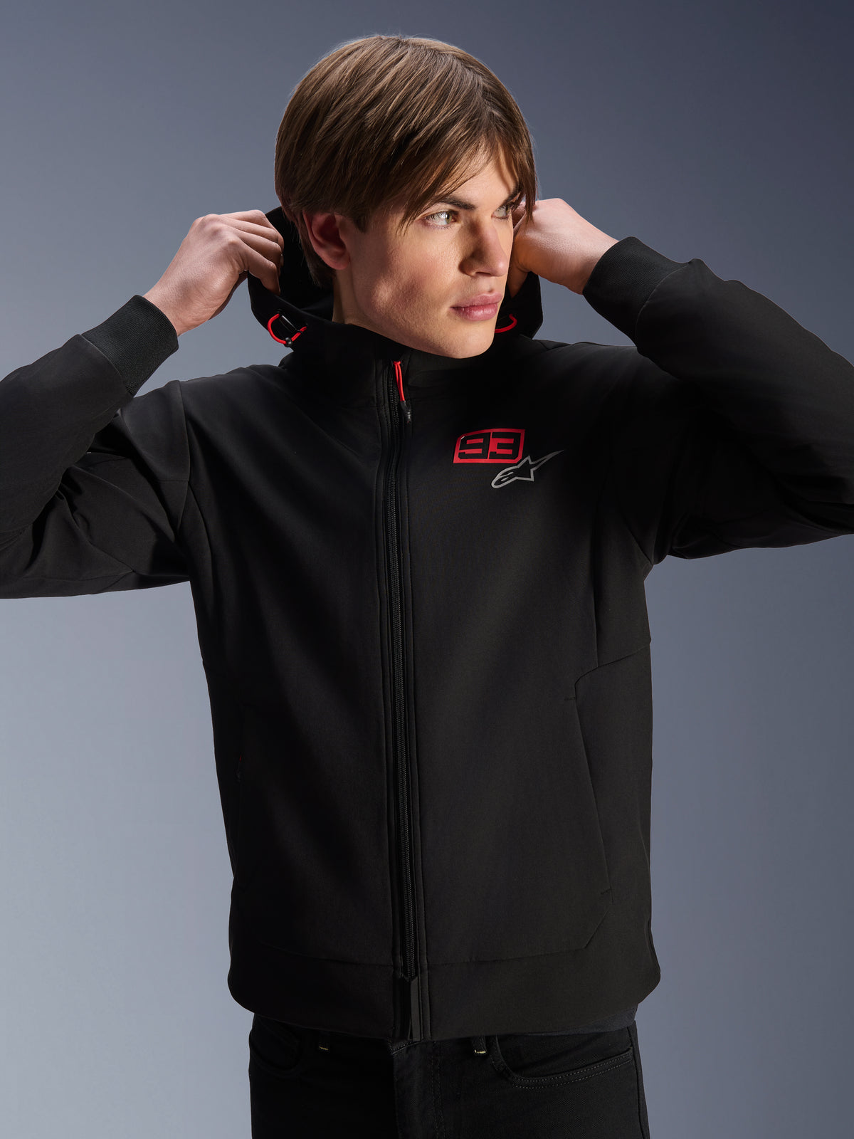 Alpinestars MM93 Radium Tech Hoodie, giacca da moto urban, nera con loghi rossi e argento, indossata da un modello, con cerniera integrale e polsini a coste, abbigliamento motorsport casual lifestyle