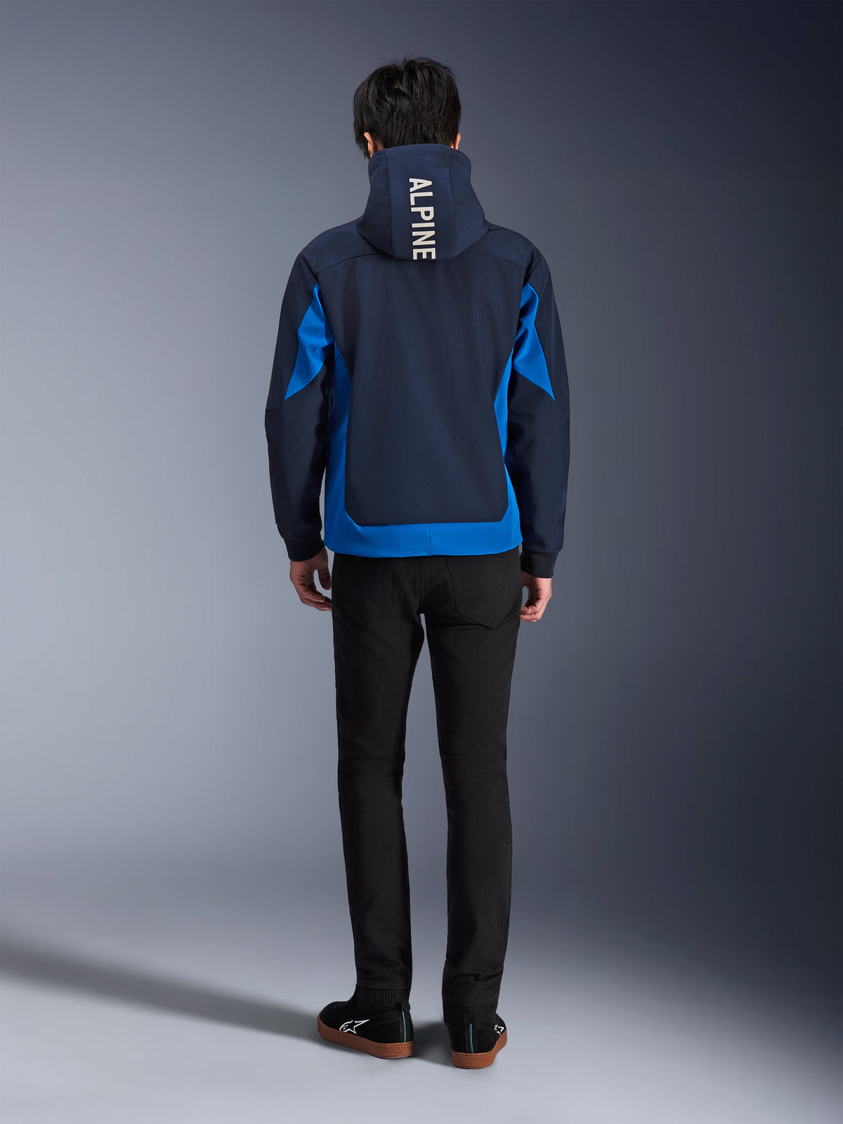 Alpinestars Radium Tech Hoodie, Night Navy e Royal Blue, vista posteriore che mostra il branding verticale 'ALPINE' sul cappuccio, pannelli laterali e orlo blu royal, felpa da moto urbana casual con guscio 3L antivento, indossata con pantaloni neri