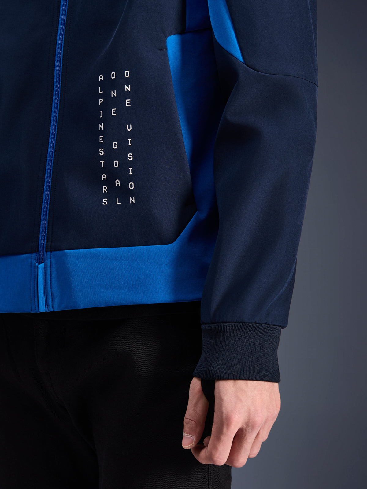 Alpinestars Radium Tech Hoodie, felpa da moto urban, Night Navy e Royal Blue, dettaglio ravvicinato del pannello laterale con grafica testuale bianca verticale, polsino elasticizzato a coste, chiusura con zip blu