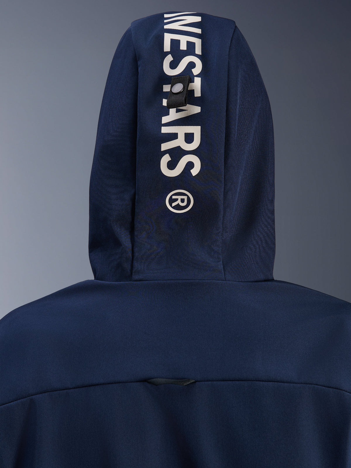 Alpinestars Radium Tech Hoodie in Night Navy Royal Blue, primo piano del cappuccio posteriore con branding Alpinestars verticale bianco e sistema di fissaggio ad asola, abbigliamento tecnico da moto urbano.