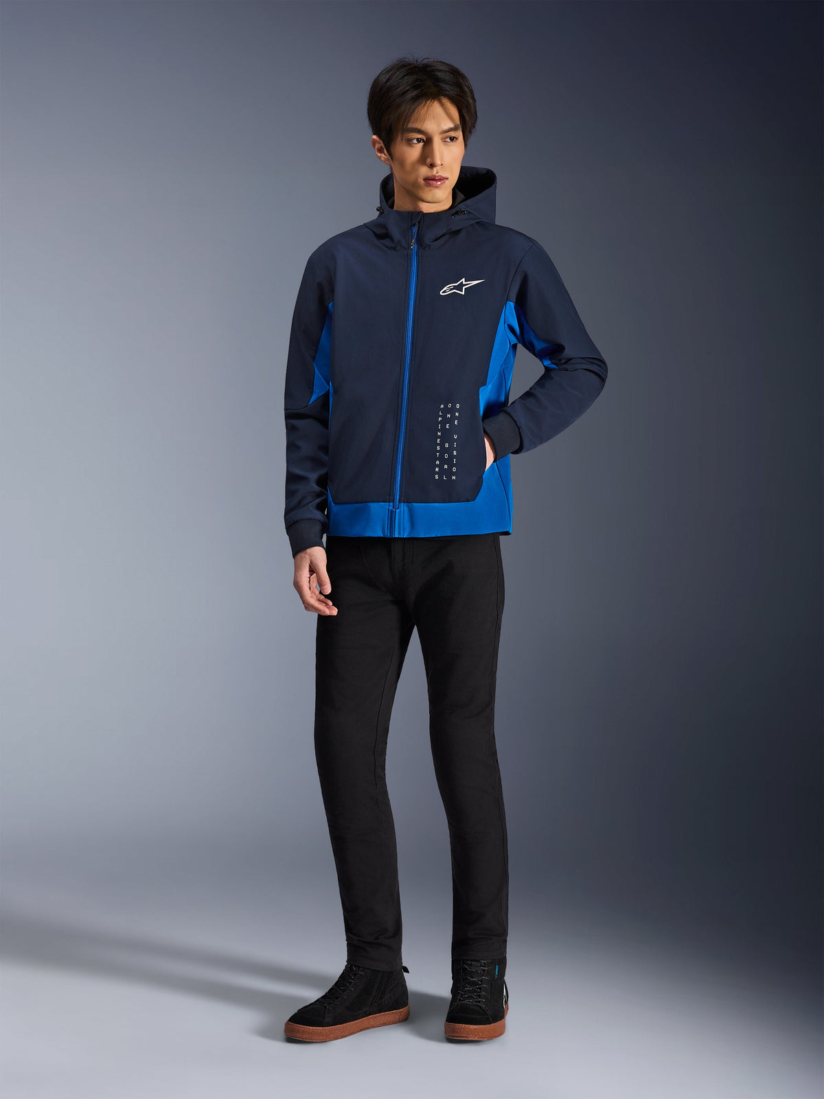 Alpinestars Radium Tech Hoodie, giacca da moto urbana, blu notte e blu reale, indossata con pantaloni neri e sneakers nere, con logo Alpinestars bianco sul petto e scritte verticali, vestibilità atletica casual per la guida in città