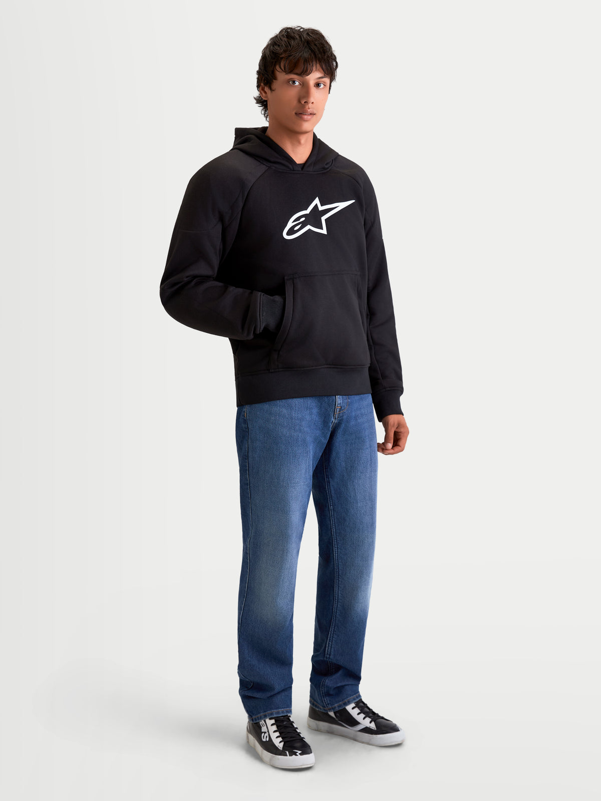 Alpinestars Felpa Con Cappuccio Ageless, felpa da moto urbana da uomo, colore nero, vista frontale su un modello che indossa jeans in denim casual, con un logo Astar bianco in evidenza sul petto e rinforzi interni anti-abrasione