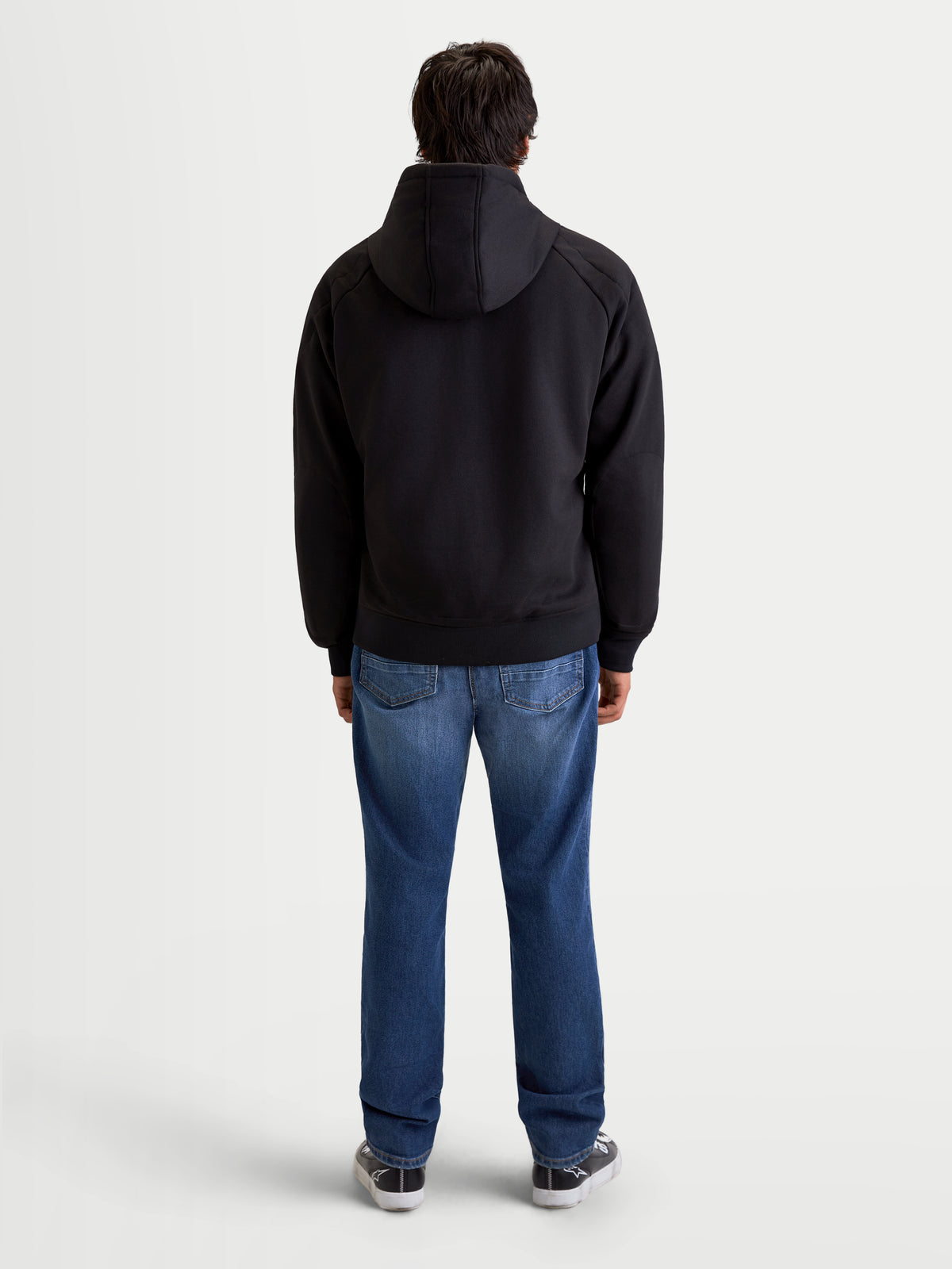 Alpinestars Felpa Con Cappuccio Ageless, felpa da moto urbana da uomo, colore nero, vista posteriore su un modello che indossa jeans e scarpe da moto casual, con cappuccio fisso e struttura protettiva in tessuto