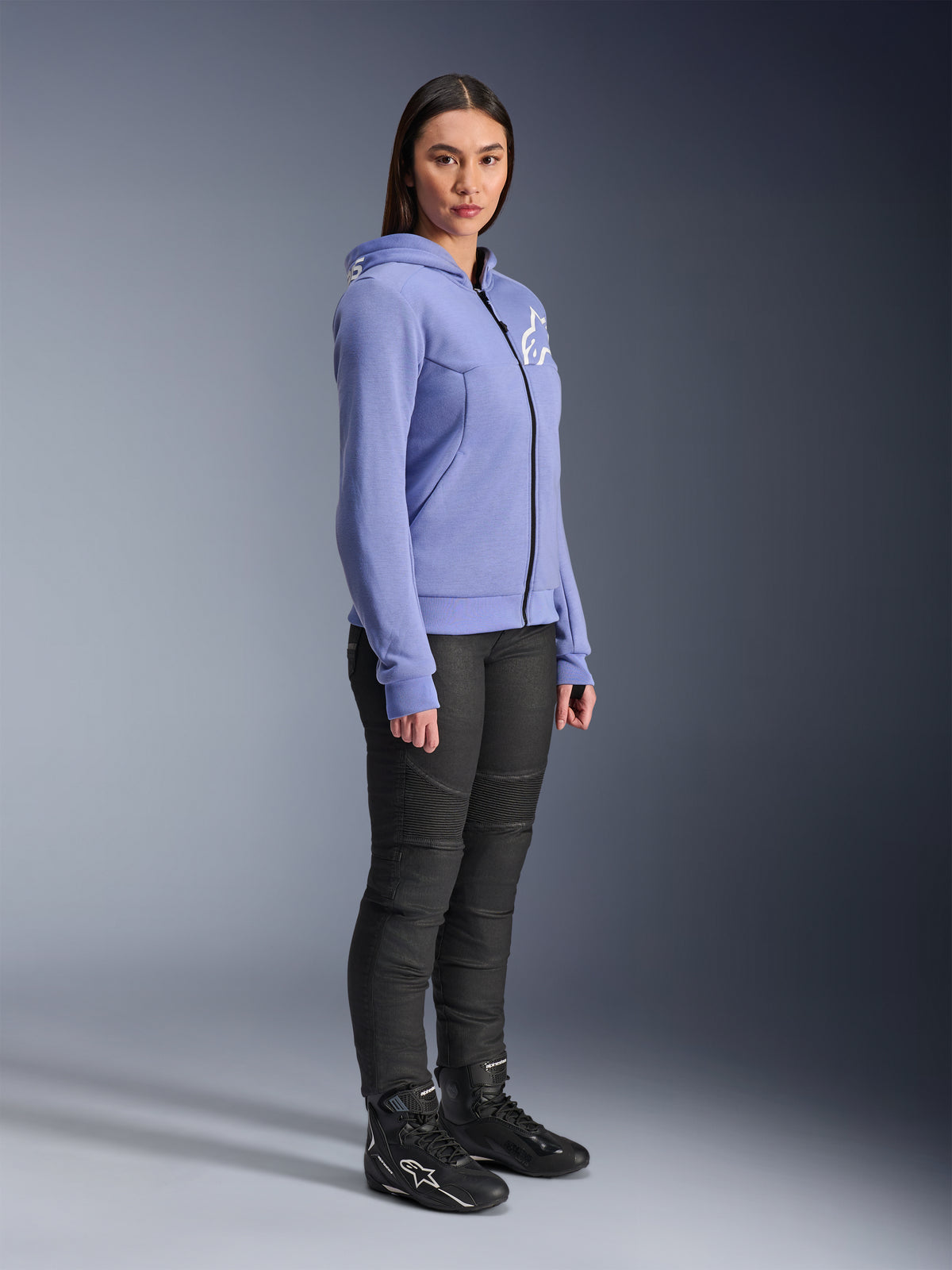 Alpinestars Stella Chrome V2 Sport Hoodie da donna, felpa da moto blu-viola con logo Alpinestars bianco sul petto, indossata da una modella con pantaloni da moto e stivali neri, abbigliamento urban riding per donna