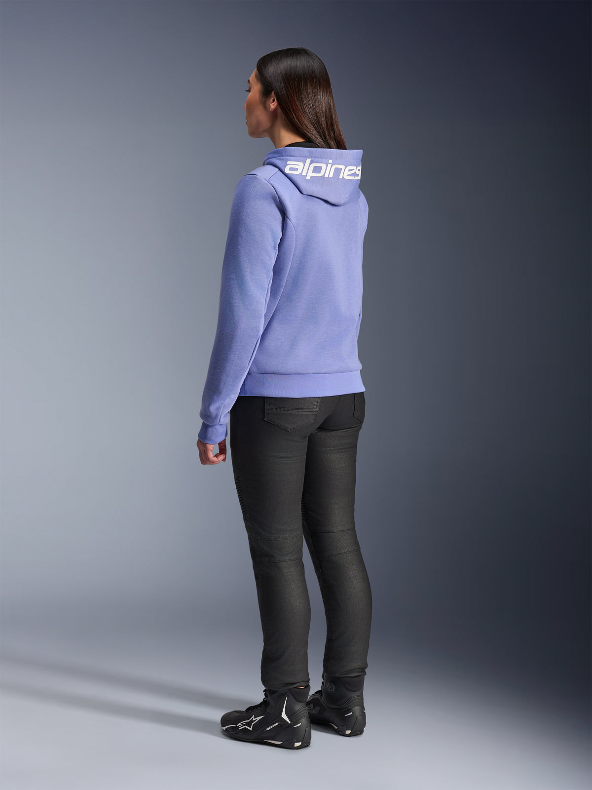 Alpinestars Stella Chrome V2 Sport Hoodie da donna, Blu Violet, vista posteriore con branding bianco sul cappuccio, indossata con pantaloni da guida neri e stivali da moto neri, abbigliamento da moto urban casual