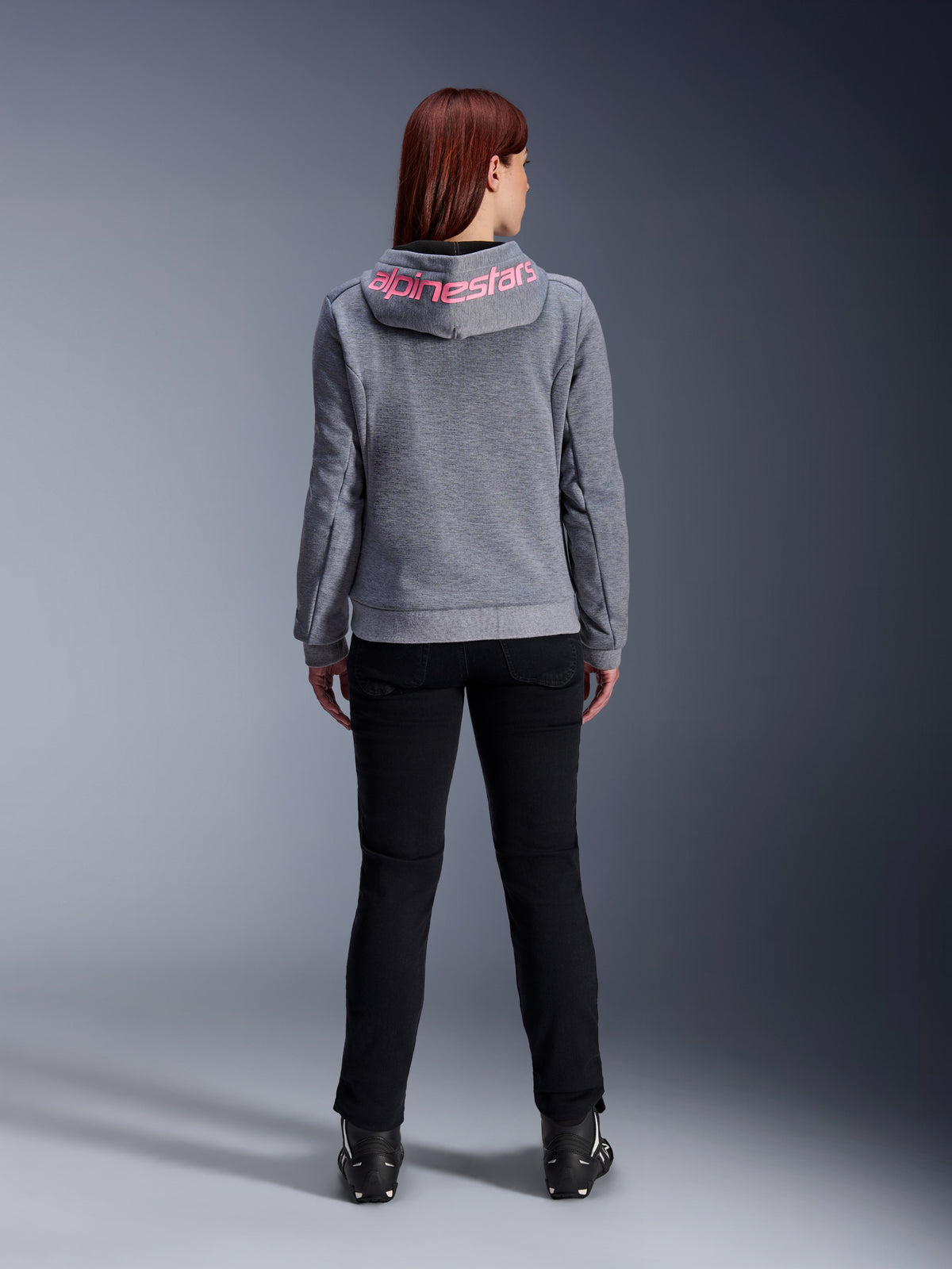 Alpinestars Stella Chrome V2 Sport Hoodie, felpa da moto da donna, grigio mélange e rosa fluo, vista posteriore con logo Alpinestars rosa sul cappuccio, indossata con pantaloni da guida e stivali neri, abbigliamento moto casual da donna