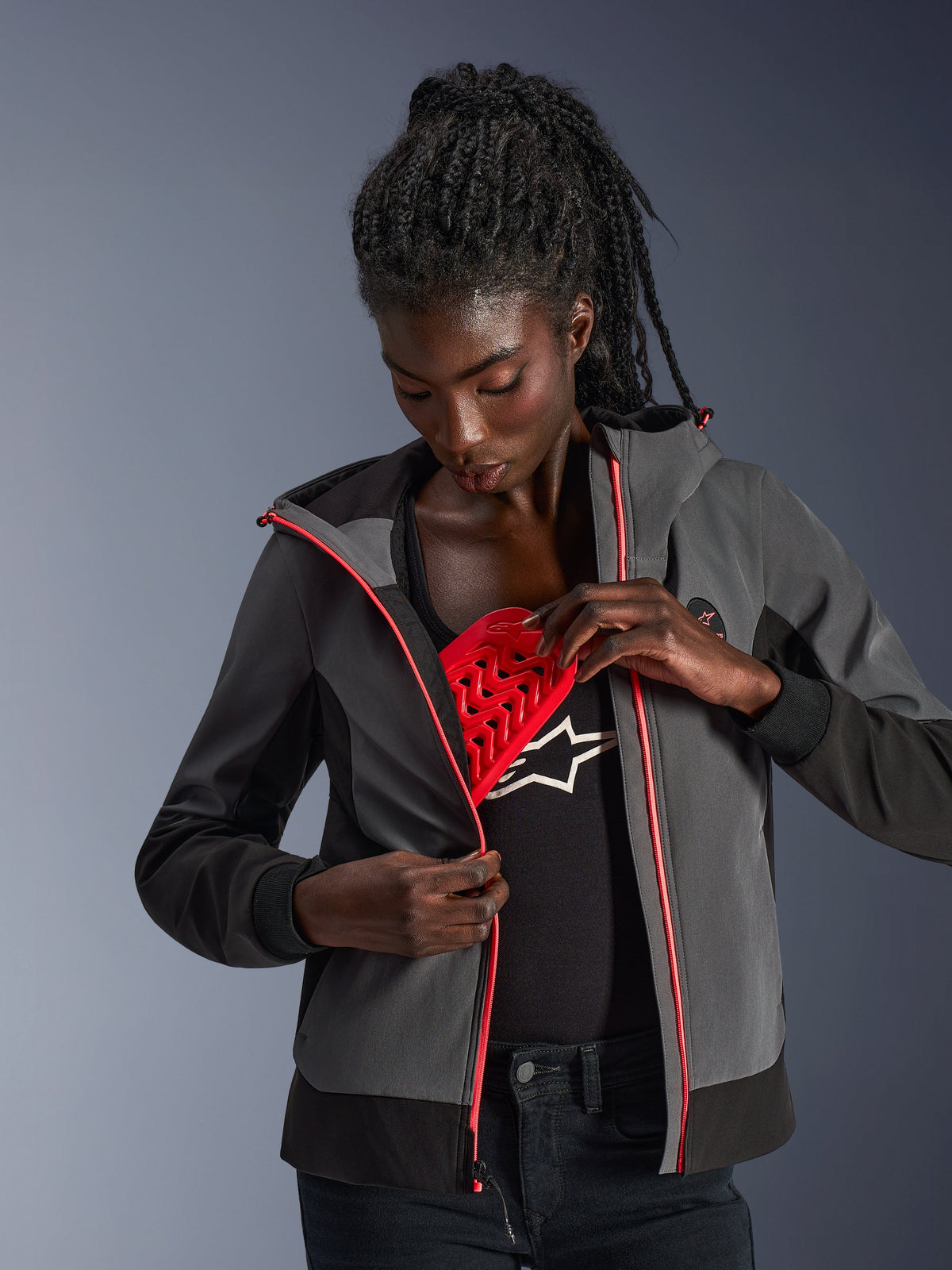 Alpinestars Stella Radium Tech Hoodie da donna, grigio scuro e nero, modella che mostra la protezione rossa rimovibile Nucleon Flex Plus, felpa da moto urbana con dettagli rosa sulla cerniera