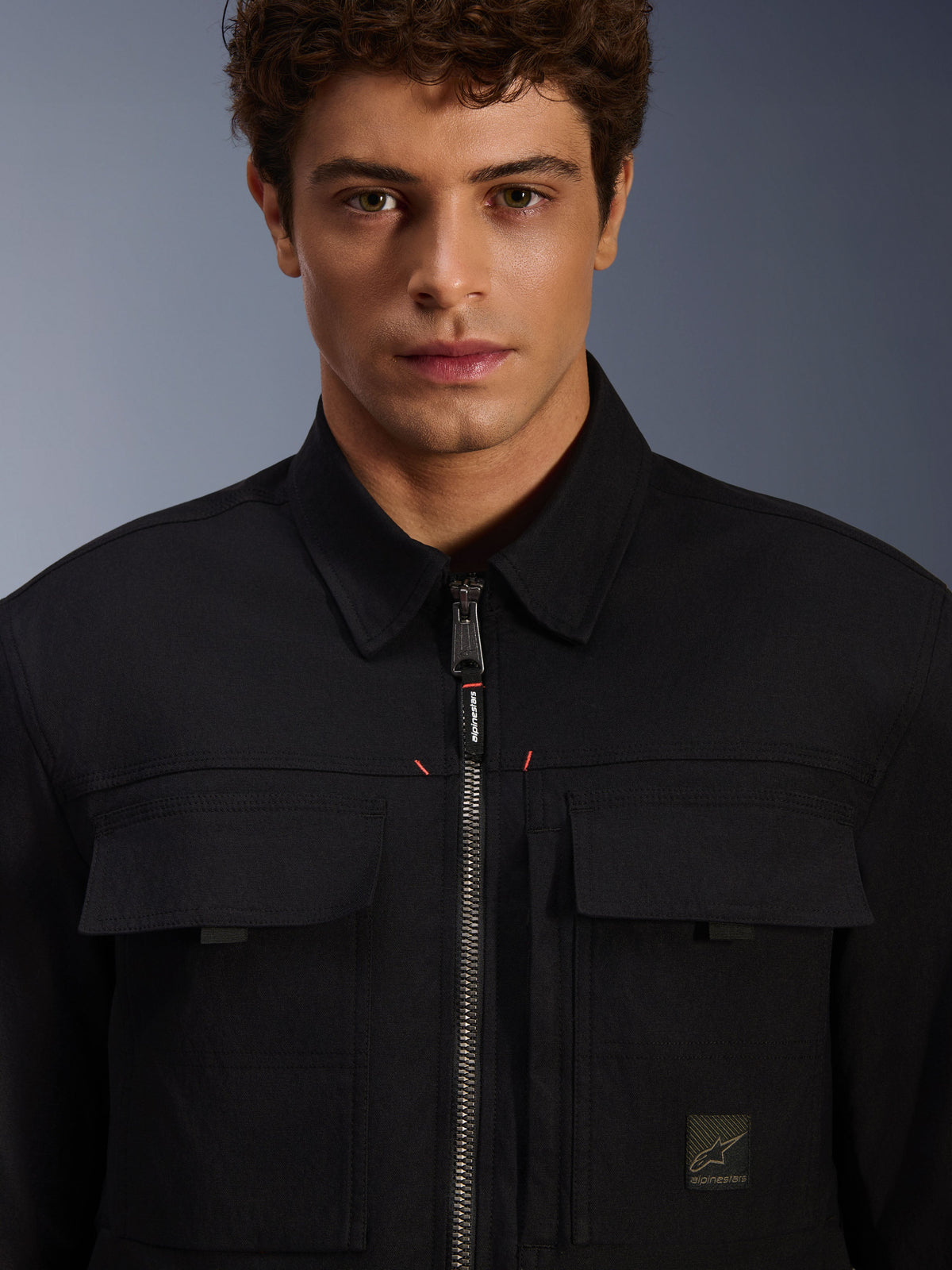 Alpinestars Bryon Water Resistant Overshirt, nero, vista ravvicinata della zip frontale e delle tasche sul petto, tessuto in canvas cerato resistente, design urbano minimalista con dettagli del brand ed etichetta logo tessuta
