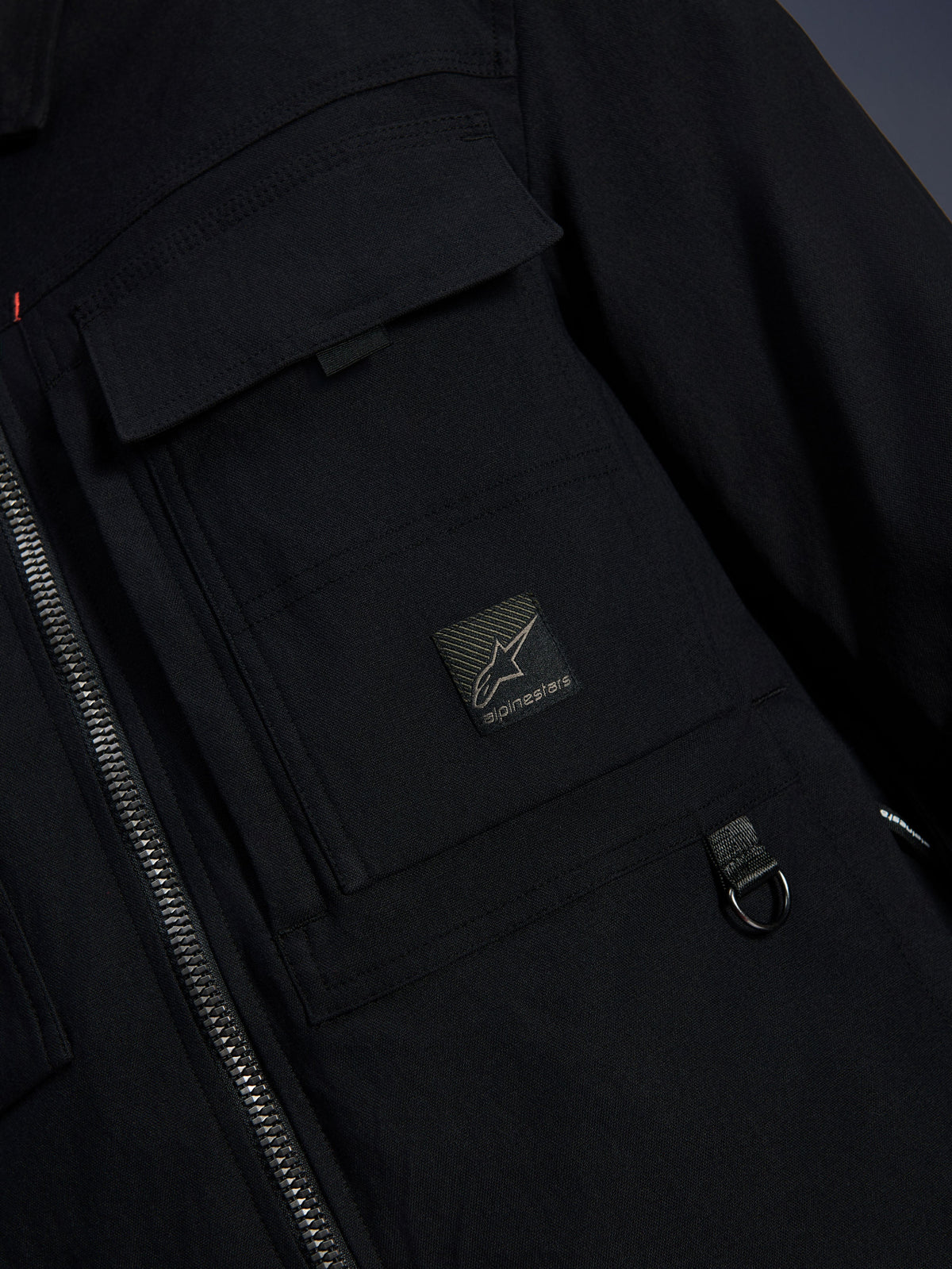 Alpinestars Bryon Water Resistant Overshirt, nero, vista ravvicinata del tessuto in tela cerata, cerniera frontale, tasca cargo sul petto con patch logo Alpinestars e dettaglio anello a D in metallo