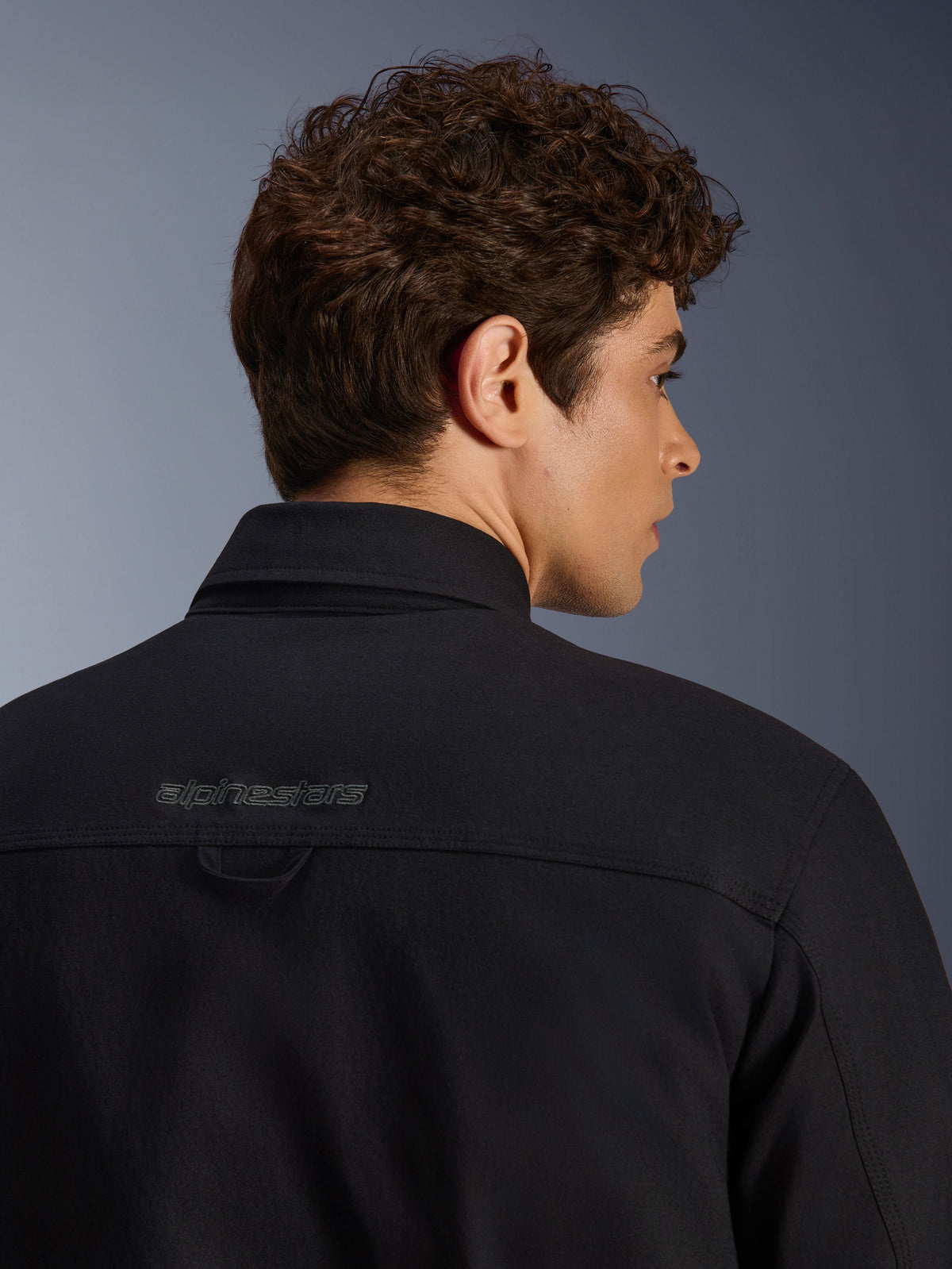 Alpinestars Bryon Water Resistant Overshirt, giacca da moto urban, nero, primo piano della zona posteriore della spalla con logo ricamato e asola per appendere, costruzione in tela cerata resistente all'acqua.