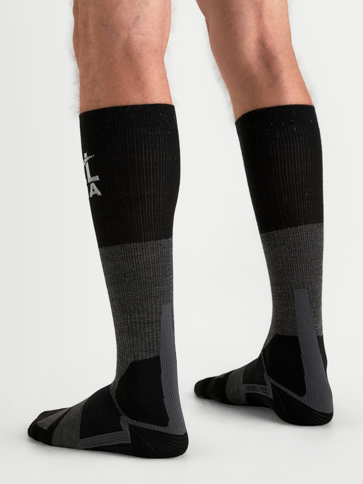 Alpinestars At 8 Merino Calzini, calzini da moto adventure lunghi, grigio scuro e nero, indossati da un modello, vista posteriore con rinforzi e marchio visibile