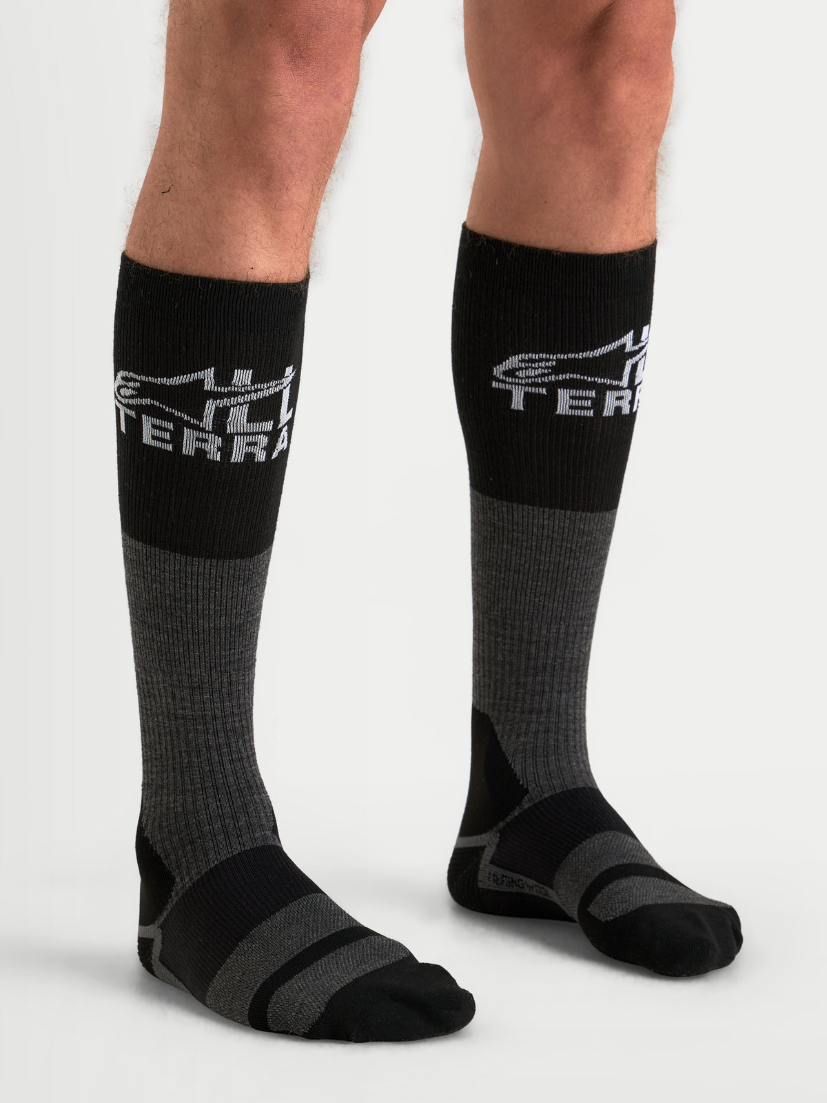 Alpinestars At 8 Merino Calzini, calzini da moto adventure lunghi al di sotto del ginocchio, grigio scuro e nero, con struttura in misto lana merino termica e marchio All Terra, indossati da un modello