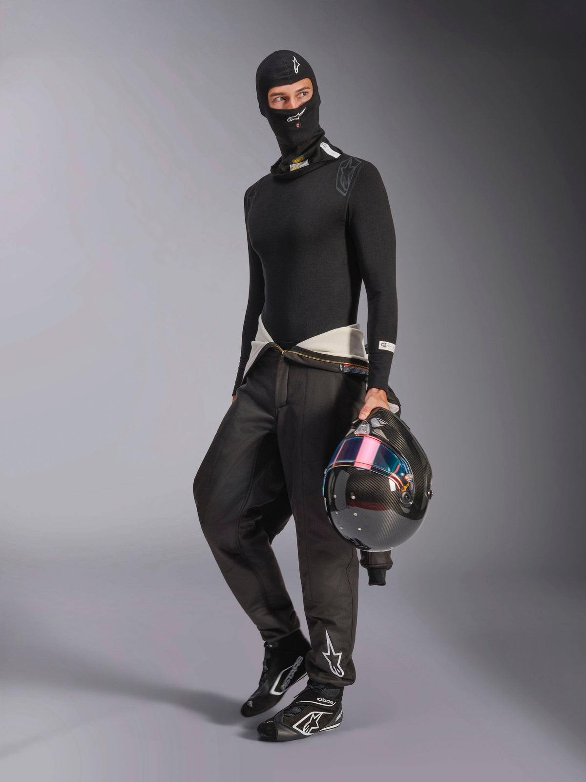 Passamontagna Alpinestars ZX Evo V3, nero, indossato da un pilota con abbigliamento intimo da corsa completo, logo bianco sulla fronte, con casco in fibra di carbonio e visiera iridescente, abbigliamento professionale ignifugo per motorsport.