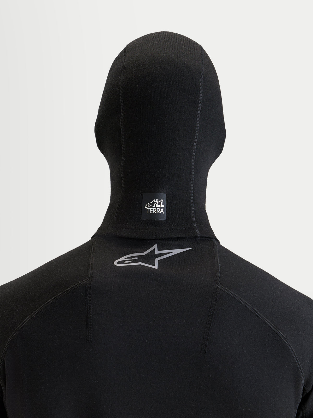 Alpinestars At 8 Merino Balaclava, passamontagna da moto nero, vista posteriore con etichetta All Terra sul collo e logo Astar riflettente sulla parte superiore della schiena, struttura in misto lana merino termica per l'avventura