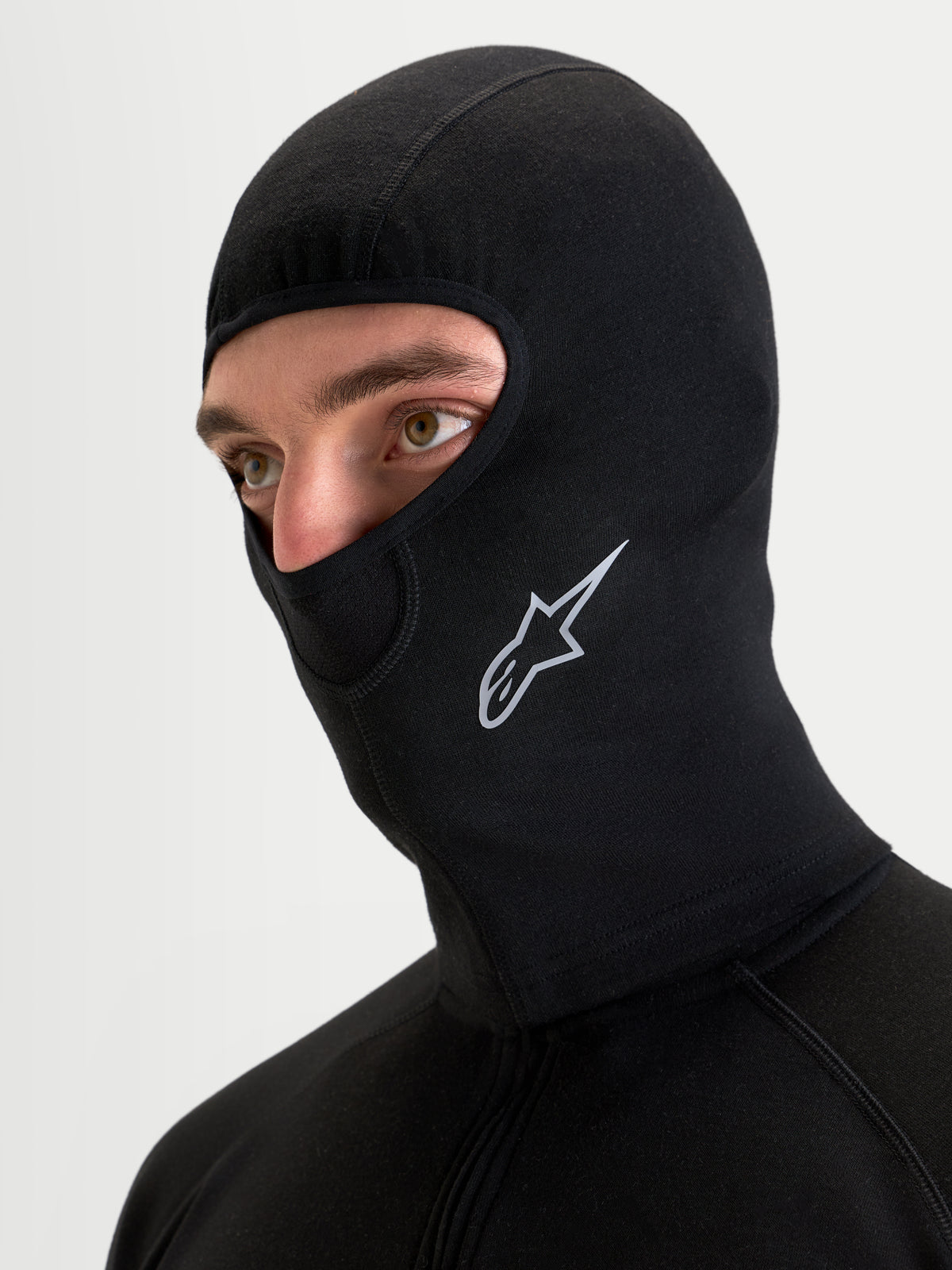 Alpinestars At 8 Merino Passamontagna da moto, passamontagna termico in tessuto misto lana merino nero indossato da un modello, con cuciture piatte e logo Astar stampato