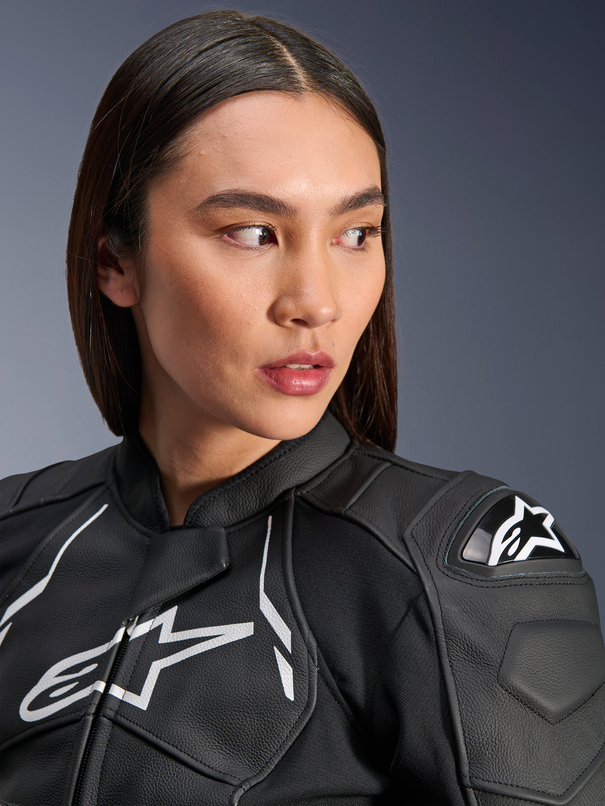 Donna che indossa la giacca in pelle Alpinestars Stella Dusk in nero e bianco, ritratto in primo piano con logo Alpinestars bianco sul petto e protezione spalla esterna DFS, struttura in pelle pregiata per gare motociclistiche su strada