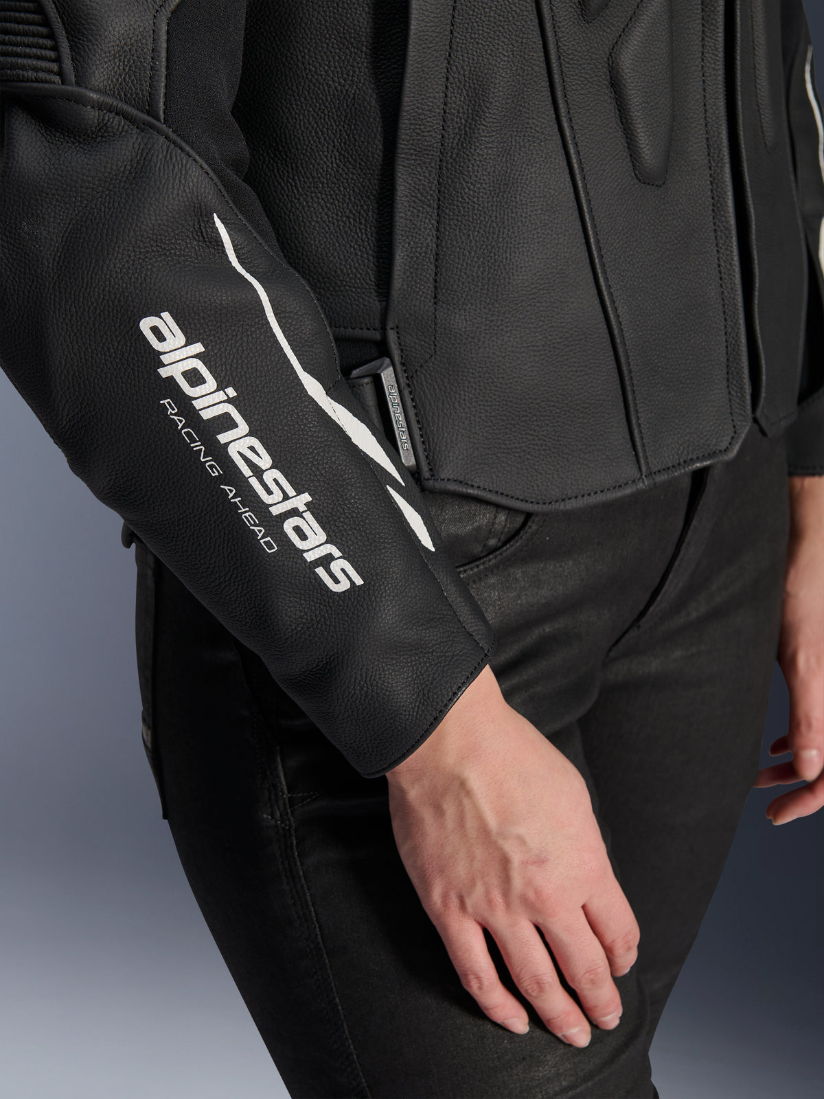 Primo piano della giacca in pelle Alpinestars Stella Dusk, giacca da moto in pelle nera da donna, con logo bianco 'alpinestars RACING AHEAD' sulla manica, texture in pelle bovina premium, indossata con pantaloni neri