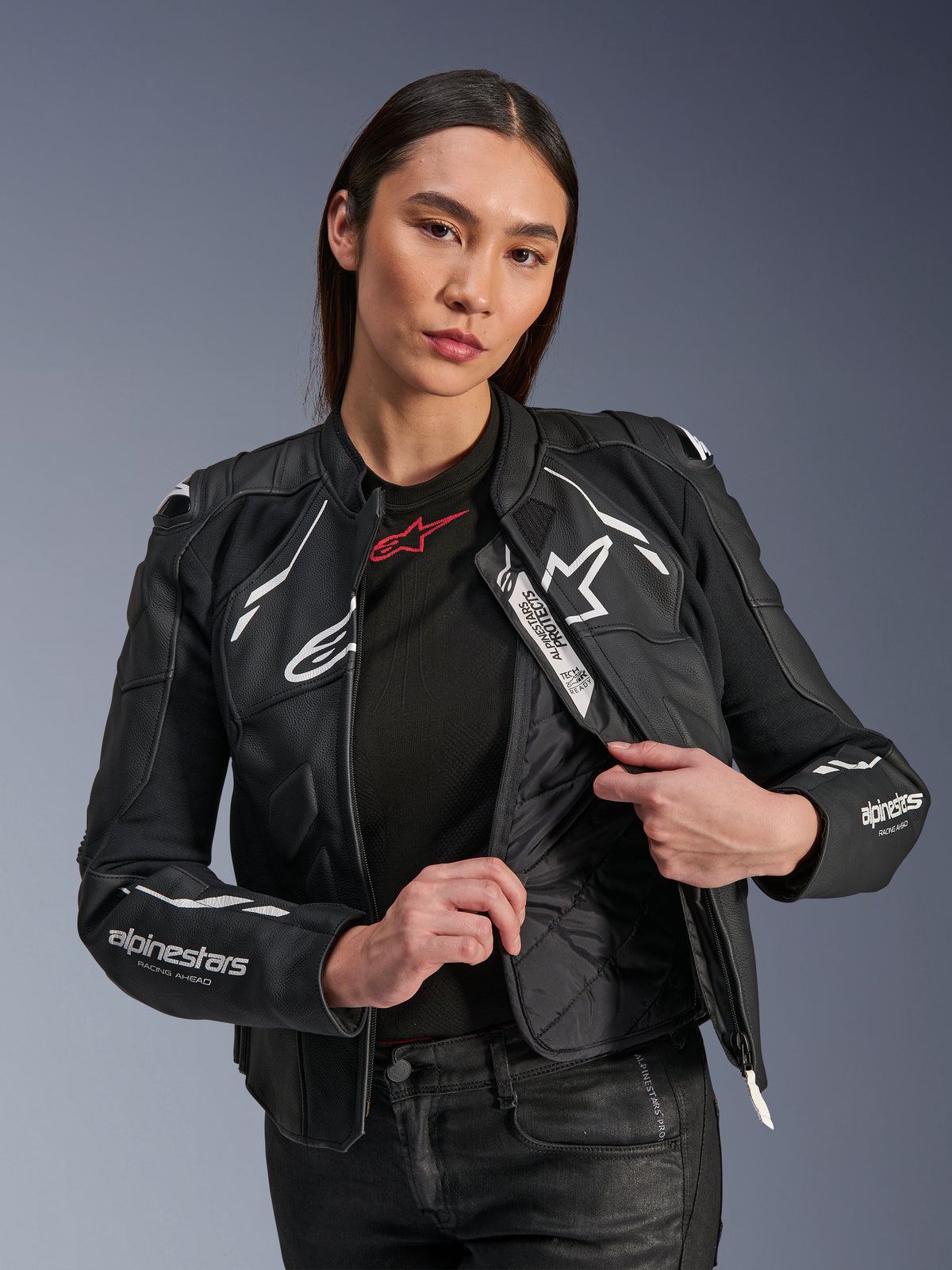 Modella che indossa la giacca Alpinestars Stella Dusk Leather Jacket in nero e bianco, con fodera termica trapuntata interna visibile, etichetta Tech-Air Ready, pelle bovina premium con logo a stella bianco e stampa 'RACING AHEAD' sulla manica