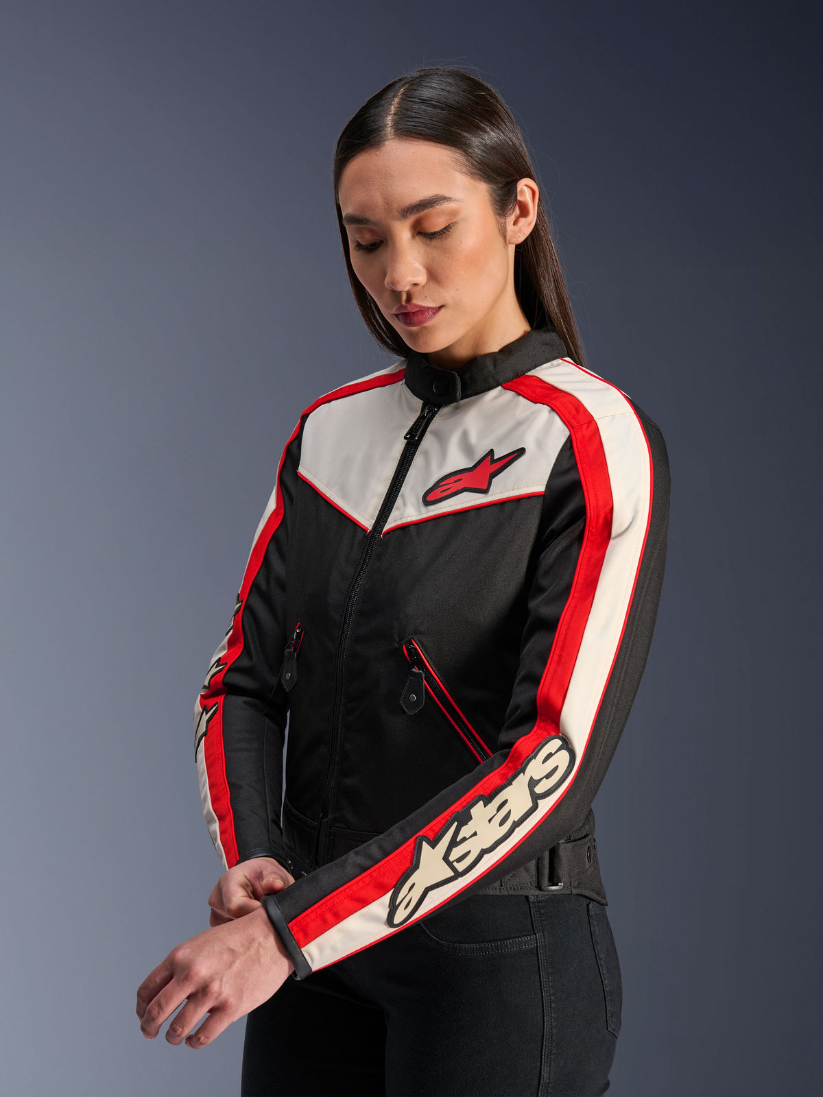 Giacca Alpinestars Stella T-Dyno WR, giacca da moto in tessuto da donna, nero, ecru e rosso brillante, design d'ispirazione vintage con logo Alpinestars rosso sul petto e marchio sulla manica, indossata da una modella in uno studio.