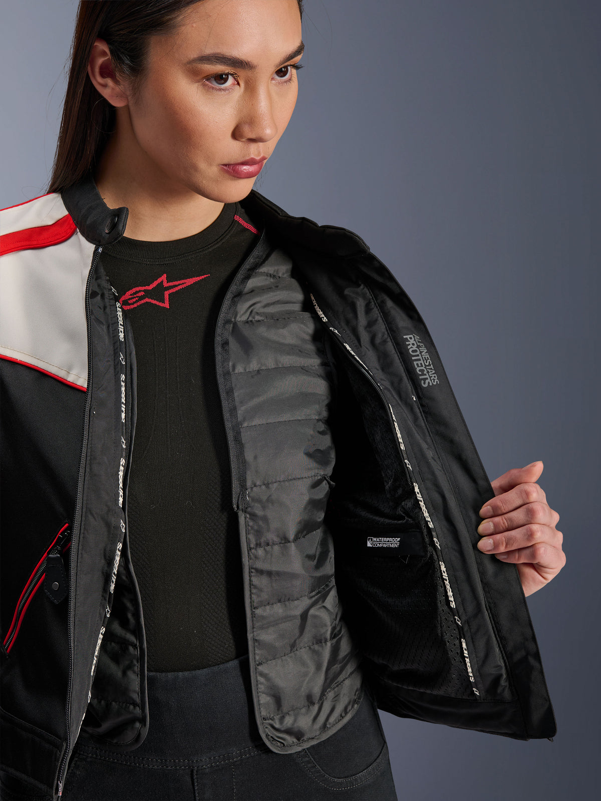 Alpinestars Stella T-Dyno WR Jacket, giacca da moto da donna, nero, ecru e rosso acceso, vista interna ravvicinata che mostra il gilet termico trapuntato staccabile, lo scomparto interno impermeabile e il marchio 'ALPINESTARS PROTECTS'.