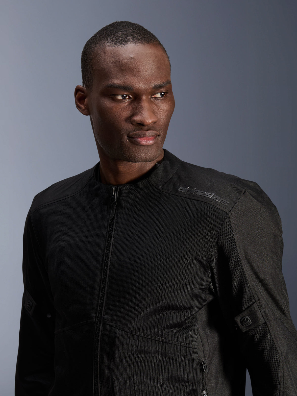 Giacca Alpinestars C-1 Air, nera, giacca da moto urbana con pannelli in rete tecnica, indossata da un modello, con logo Alpinestars a trasferimento termico sulla spalla, progettata per la ventilazione e il comfort leggero in climi caldi