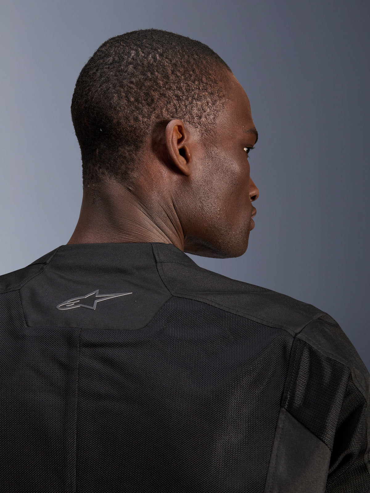 Giacca Alpinestars C-1 Air, giacca da moto nera, primo piano del retro che mostra i pannelli in rete tecnica traspirante e il logo Alpinestars riflettente sul colletto, abbigliamento da moto urbano