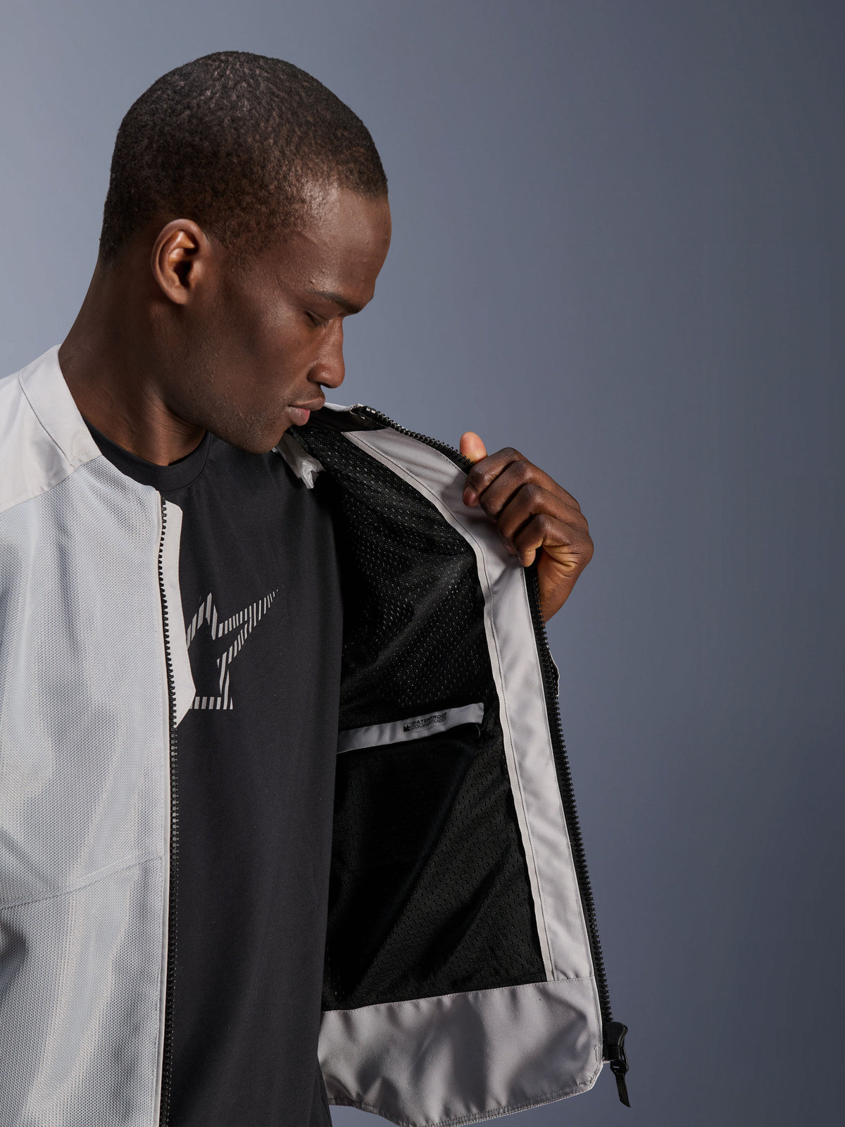 Modello che indossa la giacca Alpinestars C-1 Air in argento, aperta sul davanti per mostrare la fodera interna in mesh tecnico nero e la tasca interna impermeabile con zip.
