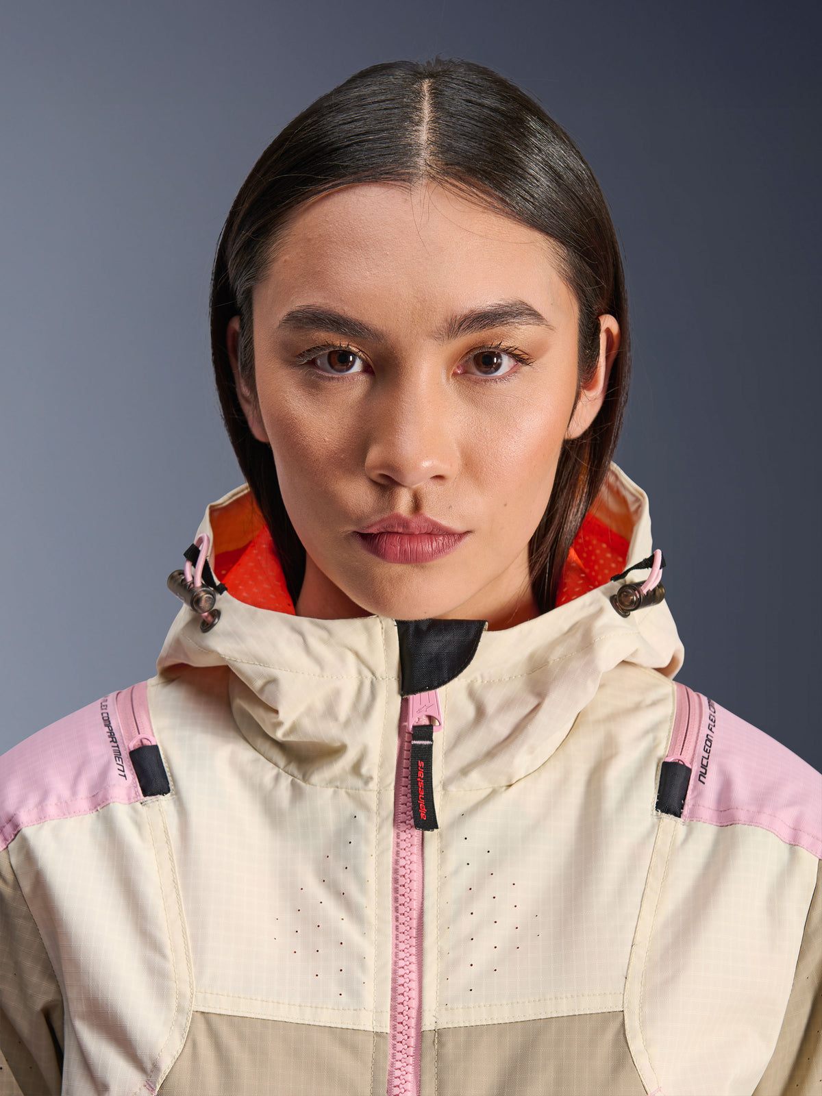 Primo piano di una modella che indossa la giacca Alpinestars Molly Air in Sand Pink Almond, con collo alto e cappuccio con fodera arancione vivace, cerniera frontale rosa, tessuto ripstop con torace traforato al laser per la ventilazione, abbigliamento protettivo da moto urbano
