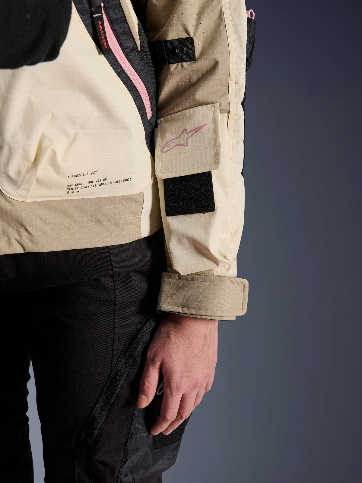 Alpinestars Molly Air Jacket, giacca da moto urban da donna, Sand Pink Almond, vista laterale ravvicinata che mostra la tasca sulla manica con logo rosa, patch in velcro nero e testo della missione del brand sulla parte bassa della schiena, materiale ripstop leggero
