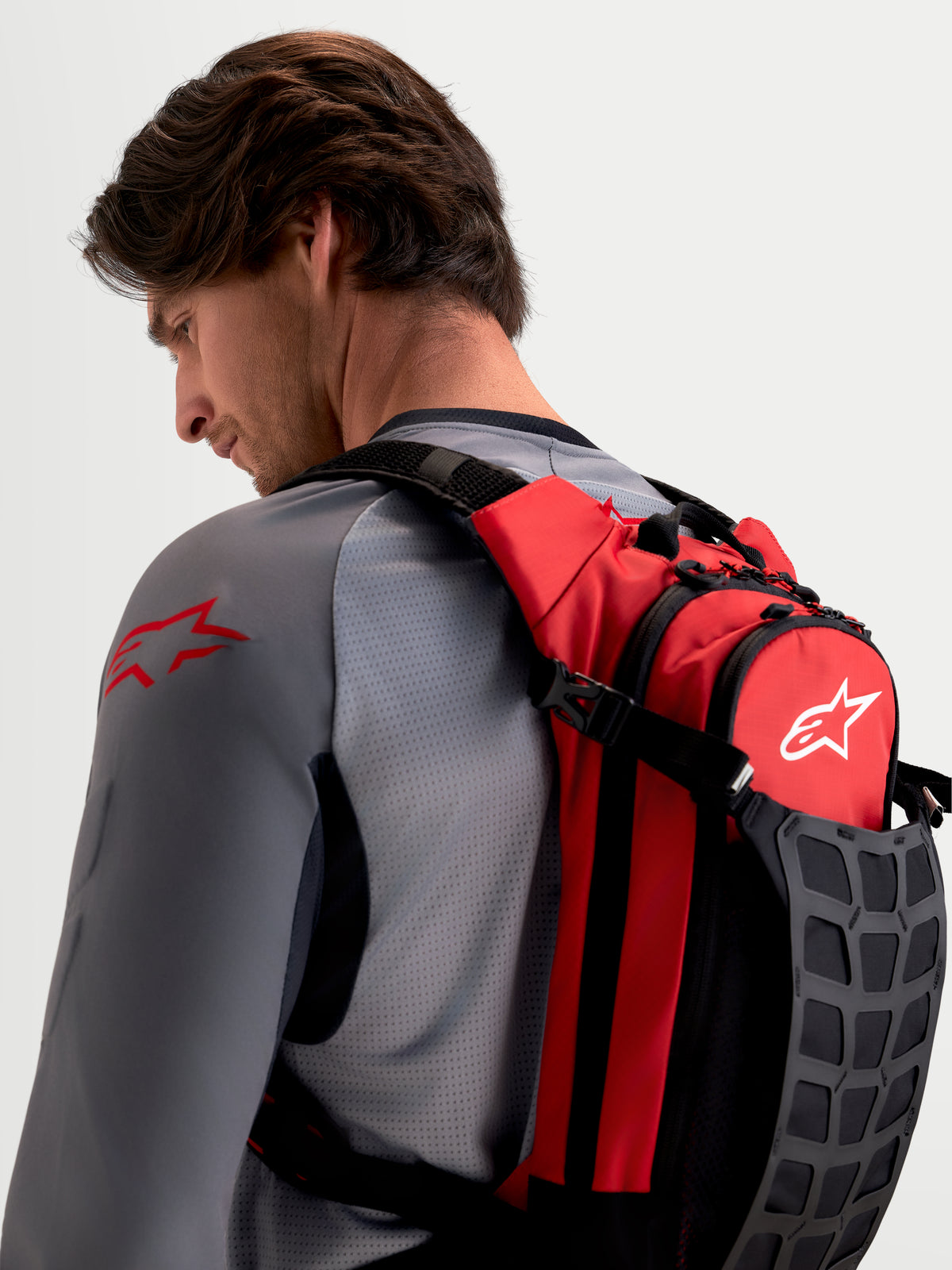 Alpinestars Zaino AT-9, zaino da motocross indossato da un modello, rosso e nero, con spallacci imbottiti e scomparti organizzati per gli essenziali in pista