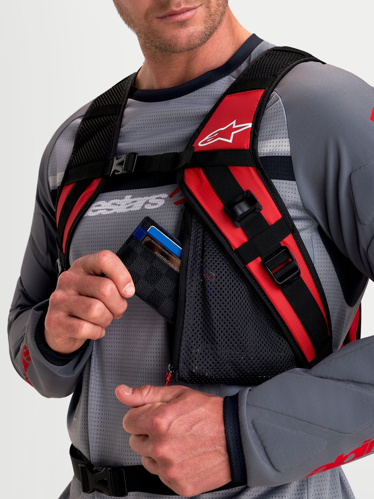 Alpinestars Zaino AT-9, zaino da motocross, nero e rosso acceso, vista in primo piano che mostra il sistema di imbracatura con spallacci imbottiti e la tasca portaoggetti in rete con cerniera indossato da un modello